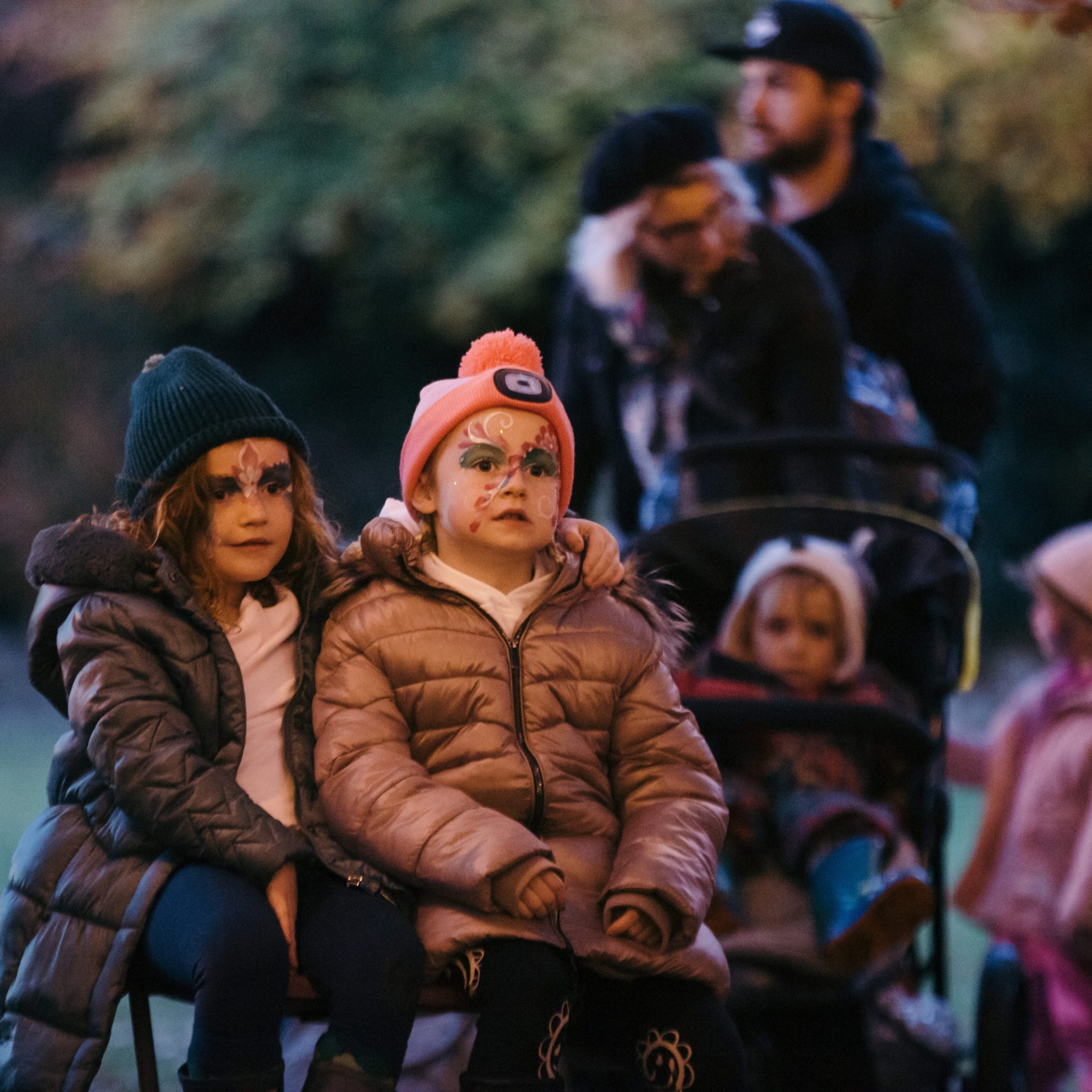 Two children with warm jackets sitting outside with faces painted