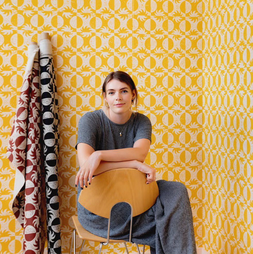 A woman with brown hair sitting in a chair looking at camera. Yellow wallpaper in background