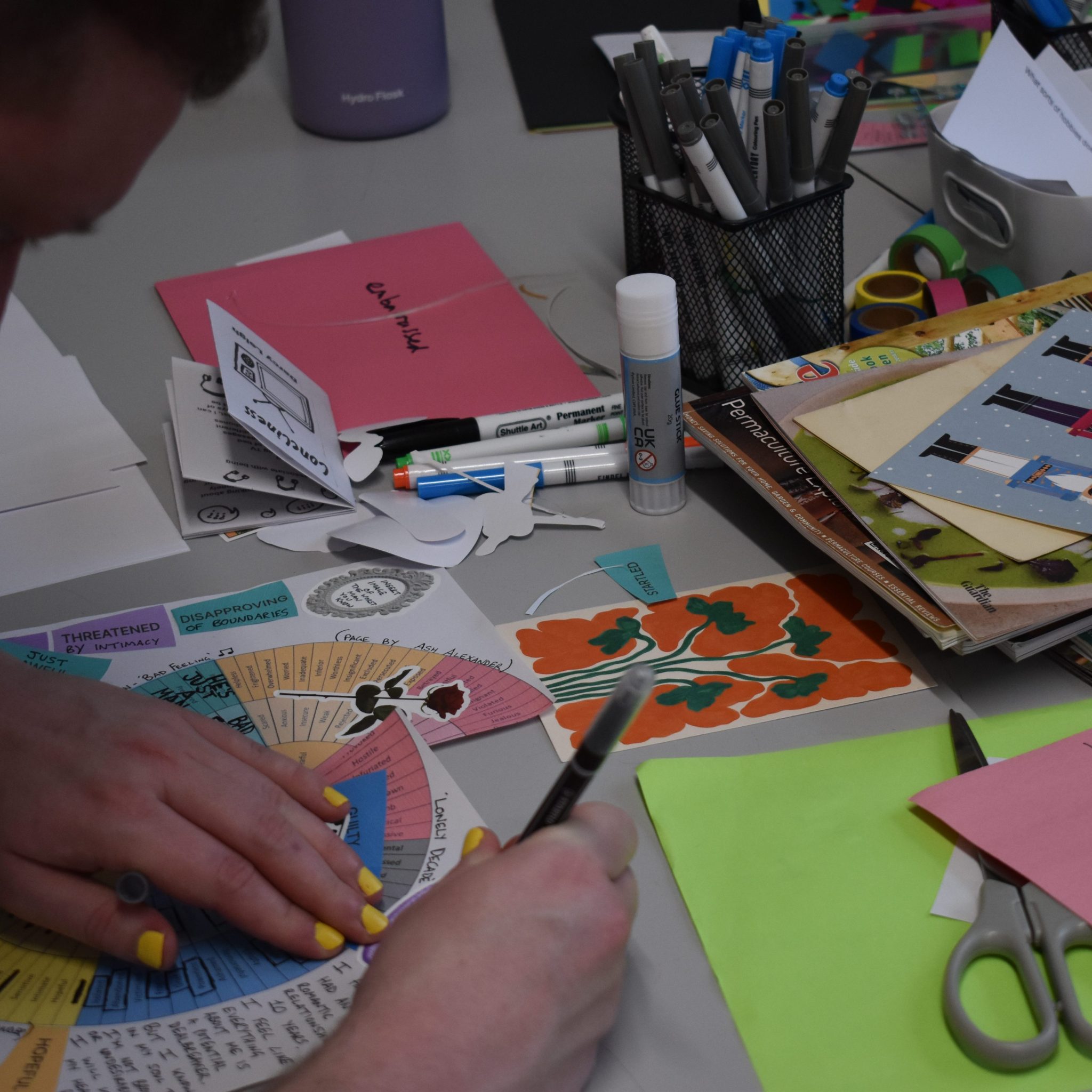 Hands with yellow nail polish drawing around materials
